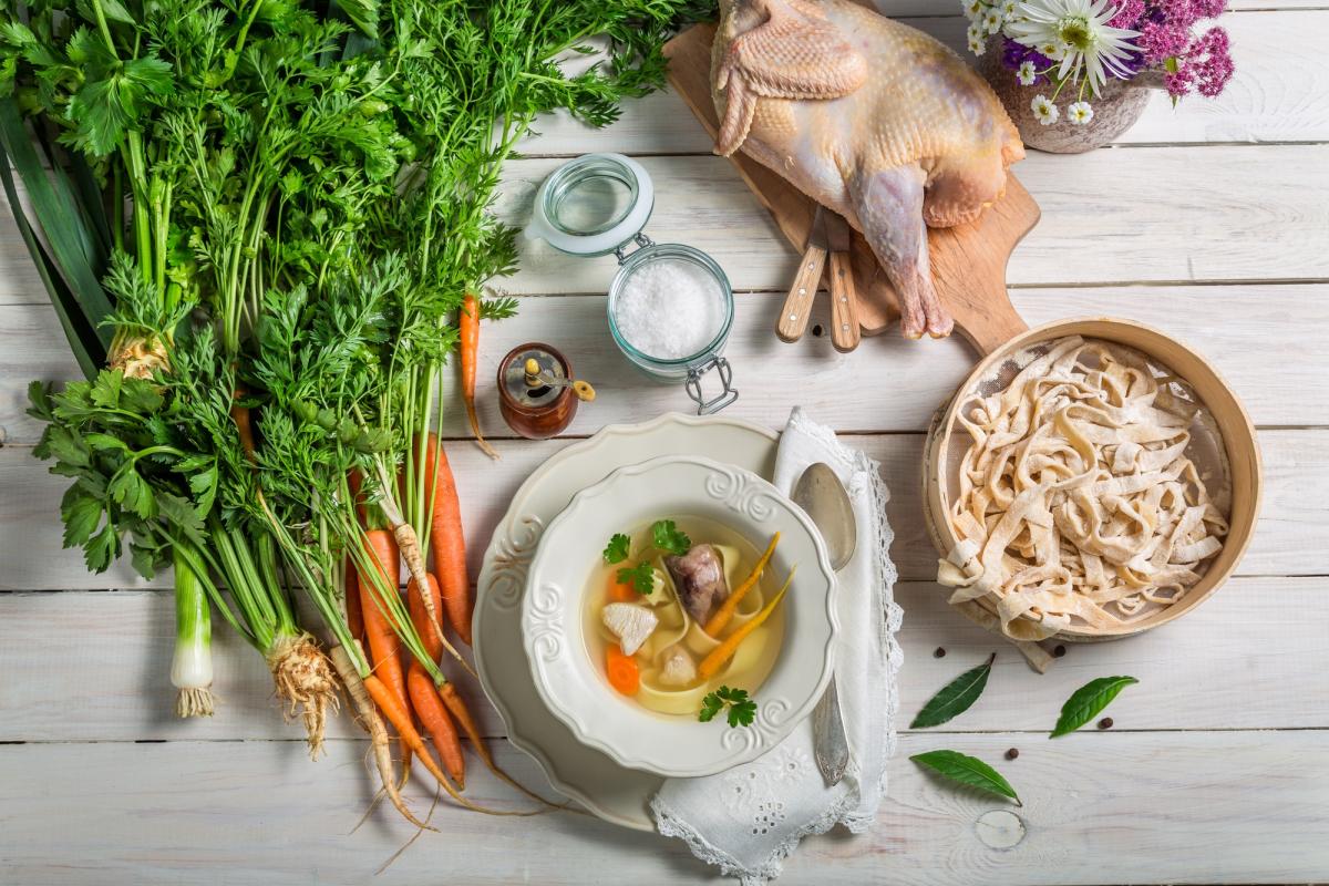 Homemade chicken noodle soup with ingredients on wooden table